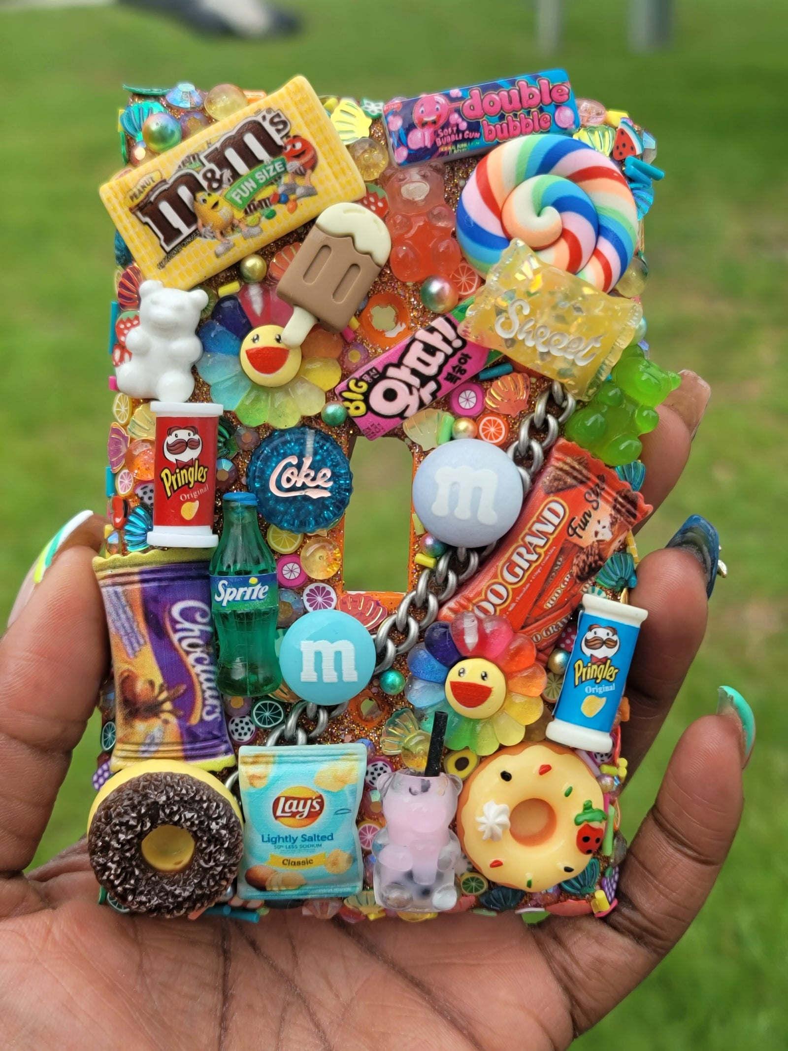 Handmade single toggle light switch cover decorated with miniature junk food and candy charms including M&Ms, Pringles, Sprite, donuts, gummy bears, and lollipops on a rainbow rhinestone background for playful nostalgic home décor