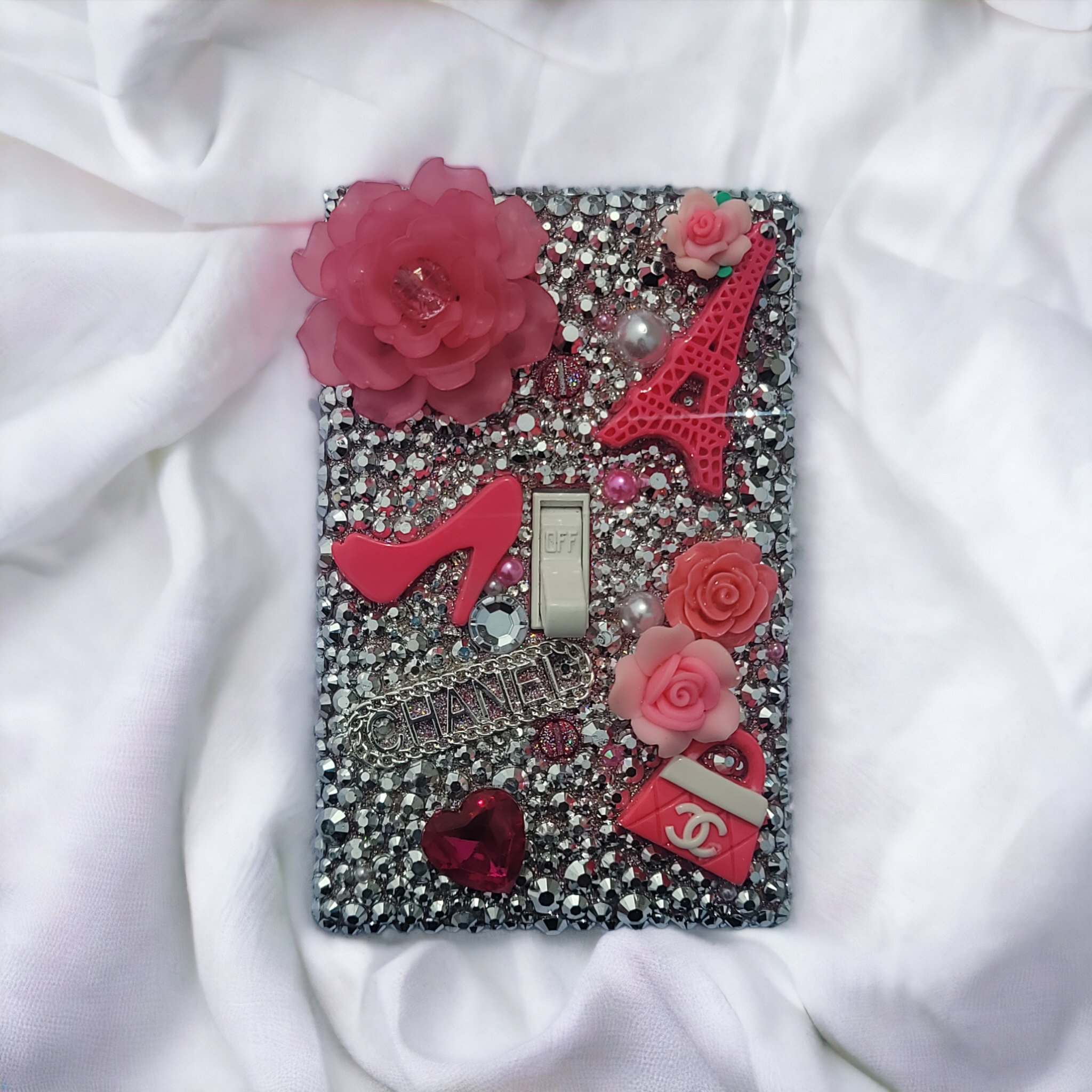 Parisian glam rhinestone switch plate covered in silver crystals with pink roses, Eiffel Tower, high heel, Chanel logo and fashion elements, handmade by Black-owned Kustom Kreationz by Kila