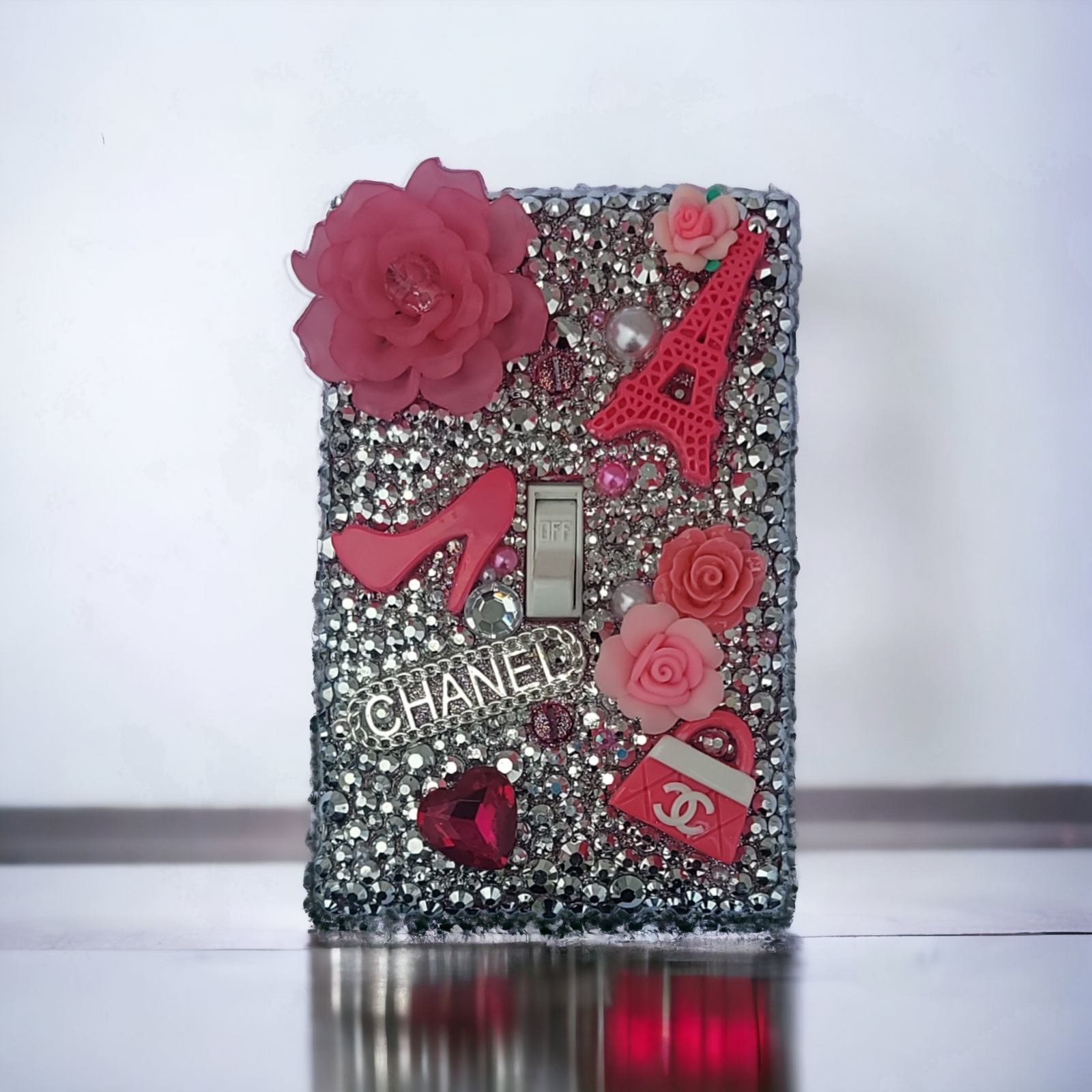 Parisian glam rhinestone switch plate covered in silver crystals with pink roses, Eiffel Tower, high heel, Chanel logo and fashion elements, handmade by Black-owned Kustom Kreationz by Kila
