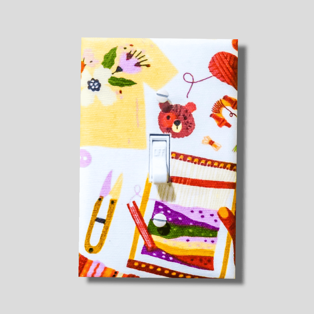 Handmade Creative Heart decorative light switch plate featuring illustrated craft supplies, cute bear, scissors, thread, buttons, and ribbons in yellow, orange, and pink—craft room switch plates from Black-owned home décor.