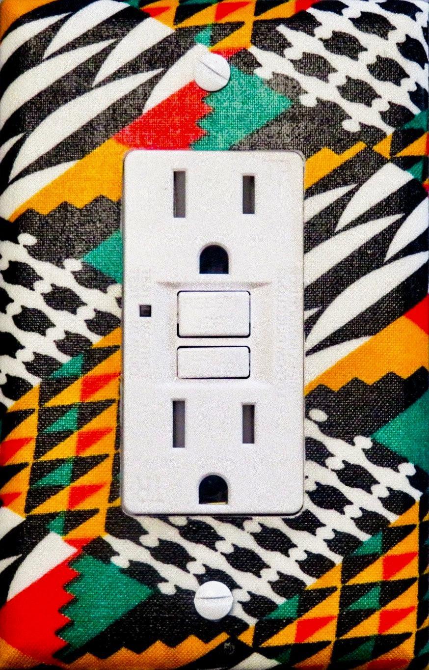 Handmade light switch cover with kente-inspired geometric patterns in forest green, red-orange, golden yellow, black, and cream featuring traditional African stepped triangles, diagonal stripes, and zigzag designs for cultural heritage home décor